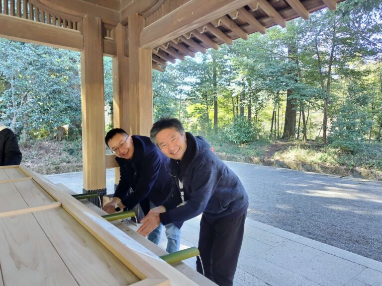 Tour guide and guest washing hands together, smiling at Meiji Shrine in Tokyo.