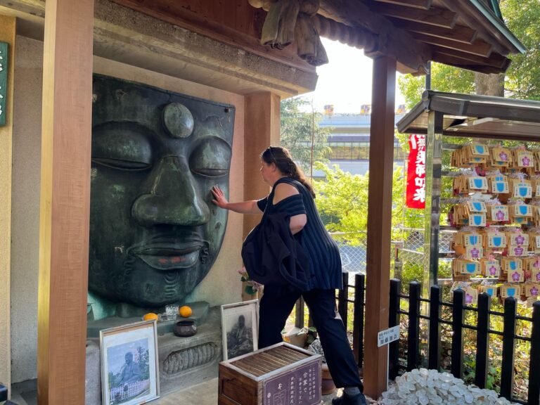 Our small group tour guest is touching the face of the Great Buddha in Ueno, Tokyo.